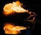 A Performer Breathes Fire, Creating A Vibrant Flame And Reflecting In Water Against A Dark Backdrop Art Print