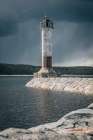 Lighthouse Standing Against Storm Clouds On Rocky Breakwater Art Print