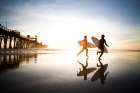 Two Surfer Run Accross The Beach At Sunset. Art Print