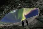 Two People Watch Northern Lights From Entrance Of An Ice Cave In The Alaska Range, Interior, Alaska. Art Print